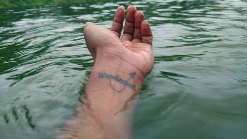 Cropped hand of man with tattoo floating on water in lake
