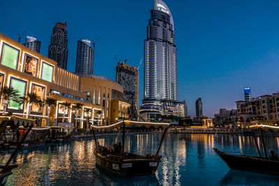 Boats in canal by illuminated buildings against clear sky