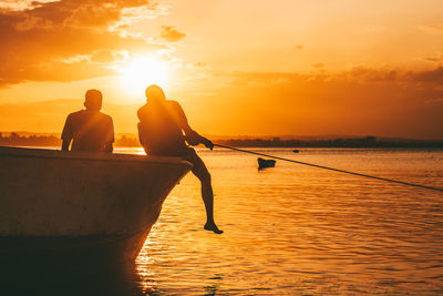 Rear view of silhouette people in sea against sky during sunset