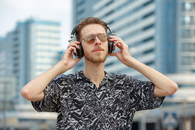Young man in headphones listening to music on the background of modern buildings