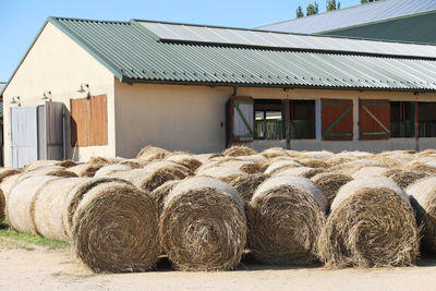 Hay bales on field by building against sky