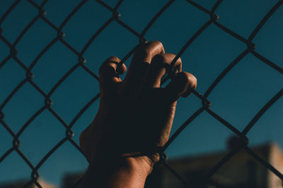 Midsection of man seen through chainlink fence against sky