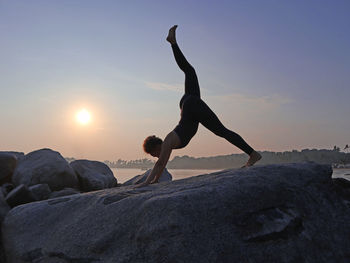 Side view of man jumping on rock against sky during sunset