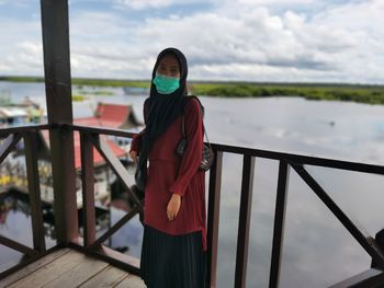 Portrait of young woman standing by railing