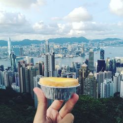 Close-up of hand holding cityscape against sky