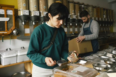 Woman filling jar with food while shopping in organic store