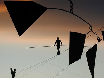 Silhouette person walking on rope against sky during sunset