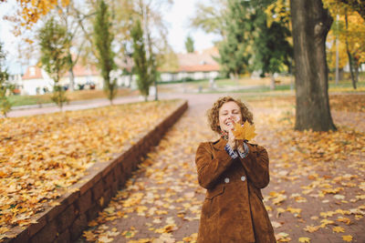 Young happy woman holding autumn leaf at park