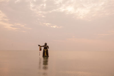 Men standing in sea against sky during sunset