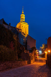 Illuminated street amidst buildings against clear sky at night