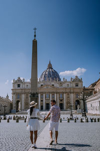 Rear view of couple holding hands standing against historical building against sky