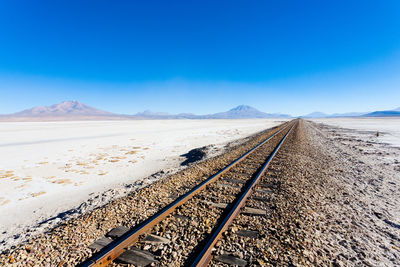 Railroad tracks in desert against clear blue sky