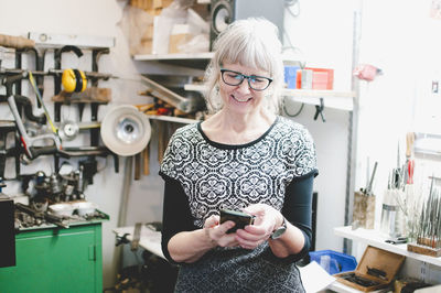 Smiling senior woman using mobile phone in jewelry workshop