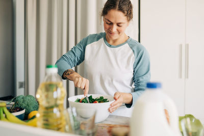 Happy smiling wife preparing vegetable summer salad in the kitchen at home.