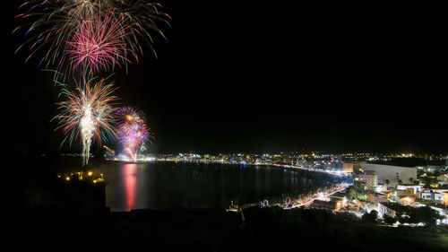 Firework display over illuminated city against sky at night