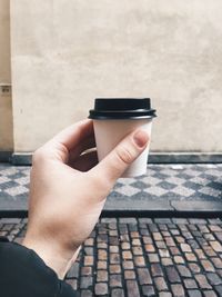 Cropped hand having coffee in disposable cup against wall