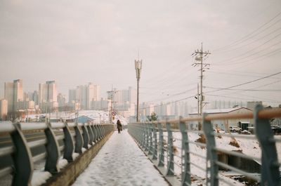 Woman walking on snowy footbridge against sky