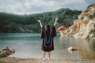 Rear view of woman with arms raised standing at beach