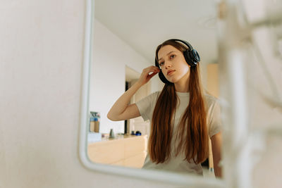 Beautiful teenage girl in headphones, looks in mirror, flirts