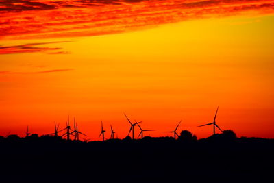 Silhouette wind turbines on land against sky during sunset