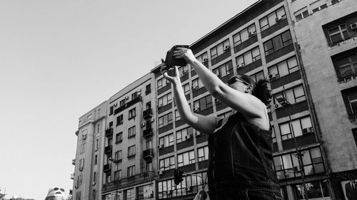 Woman photographing against building in city