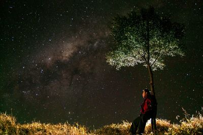 Side view of man standing by tree at night