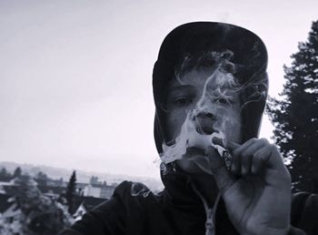 Portrait of man smoking marijuana joint against sky