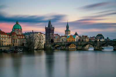 Bridge over river amidst buildings in city against sky