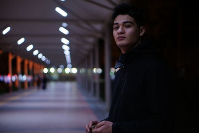 Portrait of young man standing in illuminated corridor at night