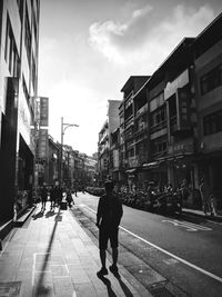 Rear view of man walking on street amidst buildings in city