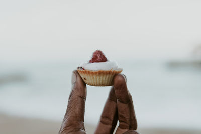 Close-up of hand holding ice cream against sky