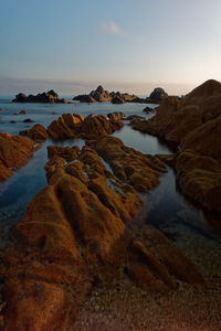 Rocks on beach against sky during sunset