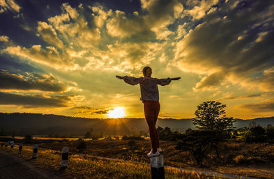Rear view of person standing on field against sky during sunset