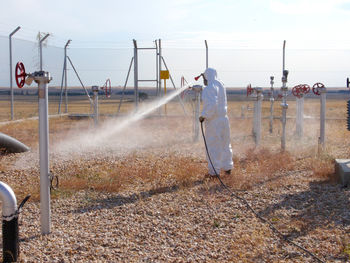 Man spraying water on field against sky
