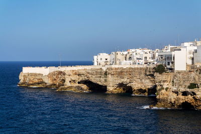 Buildings by sea against clear blue sky