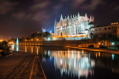 Illuminated palma cathedral by river against sky at night