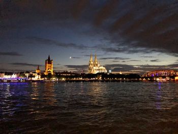 Illuminated buildings by sea against sky at night