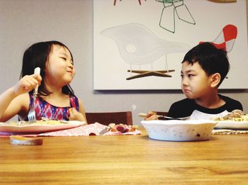 Siblings having food on table at home