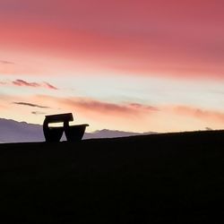 Silhouette cross on land against sky during sunset