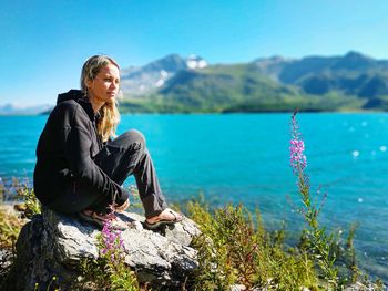 Woman sitting on rock by mountain against sky