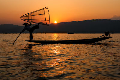 Silhouette fisherman fishing in lake against sky during sunset