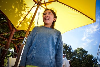 Low angle view of smiling girl standing below parasol