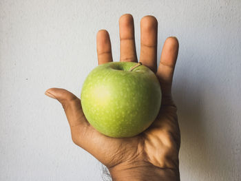 Close-up of person holding apple against wall