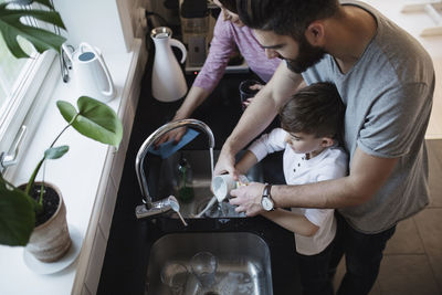 High angle view of father and son washing dishes by woman cleaning counter in kitchen