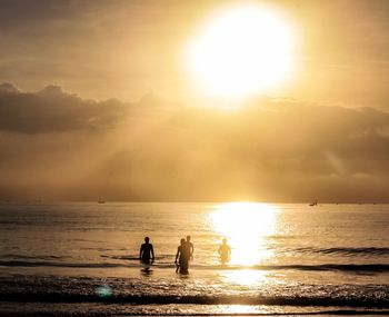 Silhouette people on beach against sky during sunset