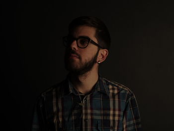 Young man wearing eyeglasses against black background