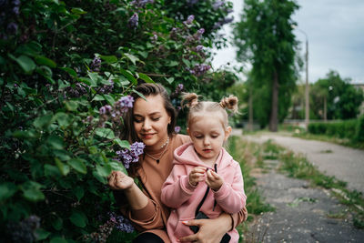 Mom hugs baby daughter lilac flowers outdoor nature