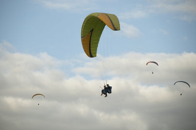 Low angle view of people paragliding against sky