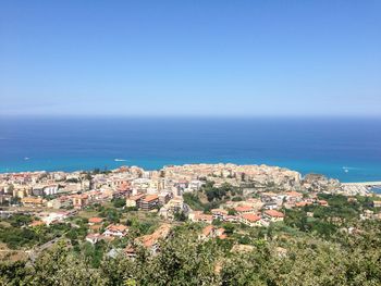 Aerial view of townscape by sea against blue sky