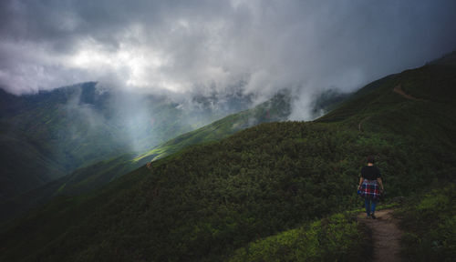 Rear view of man walking on mountain against sky